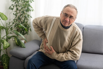 Elderly men have abdominal pain sitting on the sofa in the house. Concept Problems of the digestive tract in older people, health care.