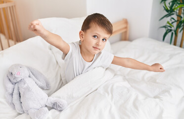 Adorable caucasian boy waking up stretching arms at bedroom