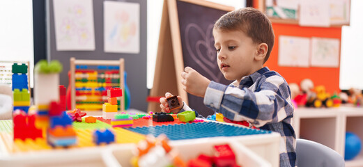 Adorable caucasian boy playing with construction blocks sitting on table at kindergarten