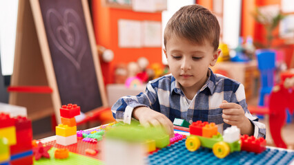 Adorable caucasian boy playing with construction blocks sitting on table at kindergarten