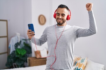Young hispanic man listning to music and dancing at bedroom