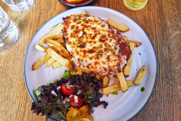 Delicious plate of italian lasagna with fried potatoes and salad wooden surface