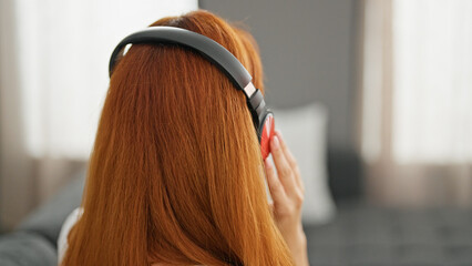 Young redhead woman listening to music sitting on sofa at home
