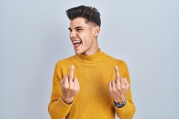 Young hispanic man standing over blue background showing middle finger doing fuck you bad...