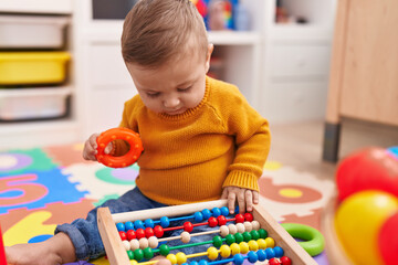 Adorable caucasian baby playing with abacus sitting on floor at kindergarten
