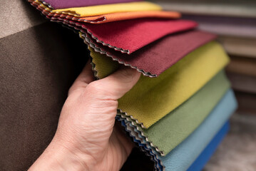 A man chooses fabric for new sofa and chairs, a whole set of upholstered furniture in the living room from a catalog, fabric samples and a man's hand close up