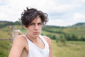 A teenage boy with a cute face but with pimples on skin is ashamed because of it, boy is relaxing in nature in the countryside, maybe he needs to see a dermatologist, he has skin problems