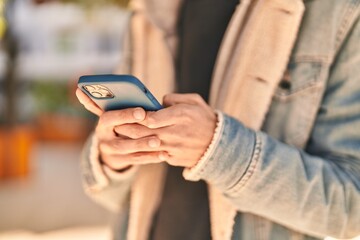 Young hispanic man using smartphone at park