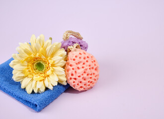 Obraz na płótnie Canvas Two interest shaped shower sponges lies on a blue washed shower towel. The yellow fresh bright flower. Copy space for text.