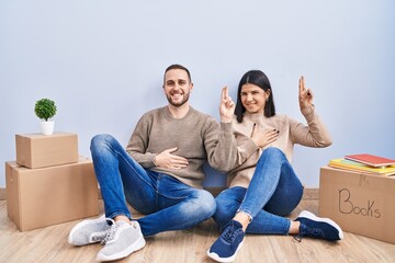 Young couple moving to a new home smiling swearing with hand on chest and fingers up, making a...