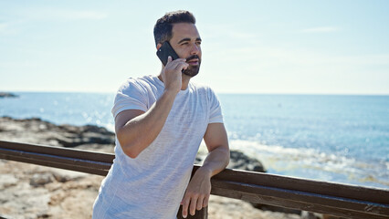 Young hispanic man talking on smartphone at seaside