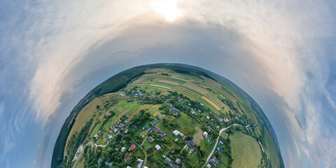Aerial view from high altitude of little planet earth with small village houses and distant green cultivated agricultural fields with growing crops on bright summer day