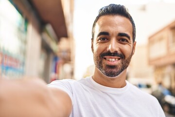 Young hispanic man smiling confident making selfie by the camera at street