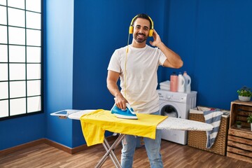 Young hispanic man listening to music ironing clothes at laundry room