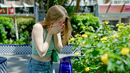 Young blonde woman smelling flowers sneezing for allergy at park