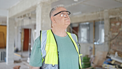 Middle age grey-haired man builder standing with relaxed expression at construction site