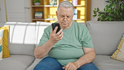 Fototapeta premium Middle age grey-haired man using smartphone sitting on sofa at home