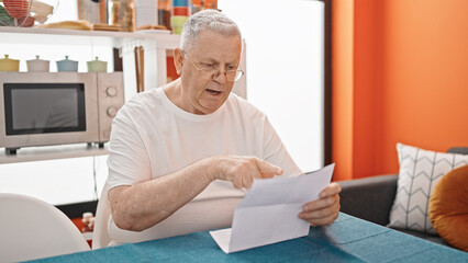 Middle age grey-haired man reading document sitting on table at dinning room