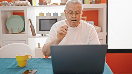 Middle age grey-haired man having video call sitting on table at dinning room