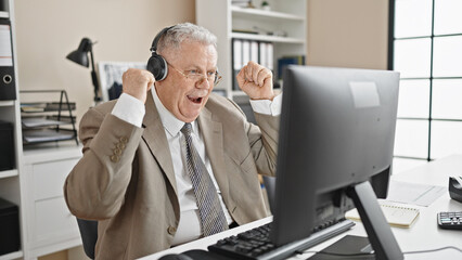 Middle age grey-haired man business worker using laptop and headphones with winner expression at office