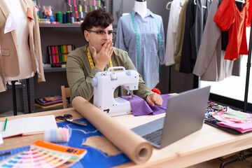 Young non binary man dressmaker designer on video call with laptop covering mouth with hand, shocked and afraid for mistake. surprised expression