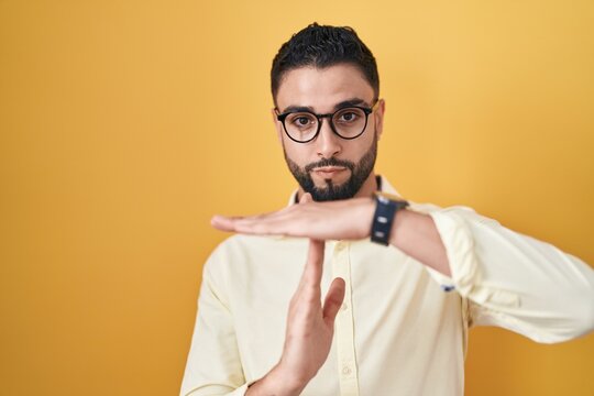 Hispanic young man wearing business clothes and glasses doing time out gesture with hands, frustrated and serious face