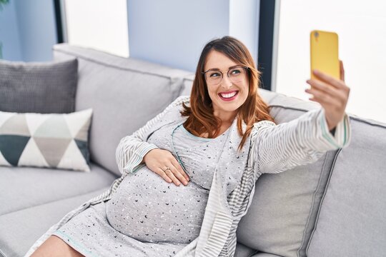 Young pregnant woman make selfie by smartphone sitting on sofa at home