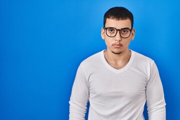 Young arab man wearing casual white shirt and glasses relaxed with serious expression on face. simple and natural looking at the camera.