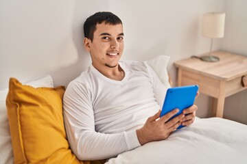 Young man using touchpad sitting on bed at bedroom