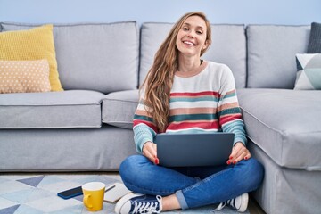 Obraz premium Young blonde woman using laptop drinking coffee at home