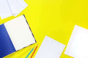 Back to school. Workspace, top view, flat lay. Open notebooks, pencils and envelopes on a yellow background. Mock-up notebooks and a set of stationery for work and study