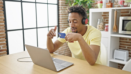 African american man having video call holding credit card sitting on table at dinning room