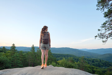 Naklejka premium Hiker woman walking on mountain footpath enjoying evening nature. Lonely female traveler traversing wilderness trail. Healthy lifestyle concept