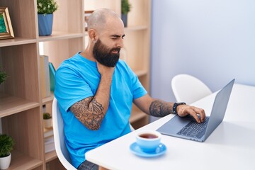 Young bald man using laptop suffering for throat pain at home