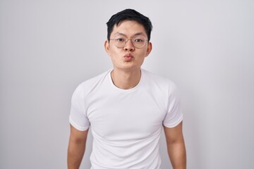 Young asian man standing over white background looking at the camera blowing a kiss on air being lovely and sexy. love expression.