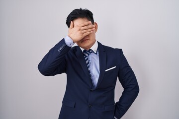 Young asian man wearing business suit and tie covering eyes with hand, looking serious and sad. sightless, hiding and rejection concept