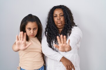 Mother and young daughter standing over white background doing stop sing with palm of the hand....