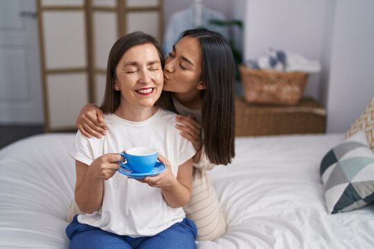 Two women mother and daughter hugging each other drinking coffee at bedroom