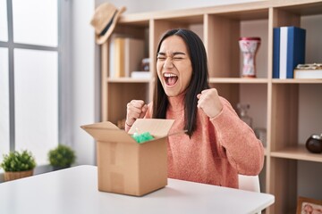 Young south asian woman opening cardboard box celebrating surprised and amazed for success with arms raised and eyes closed