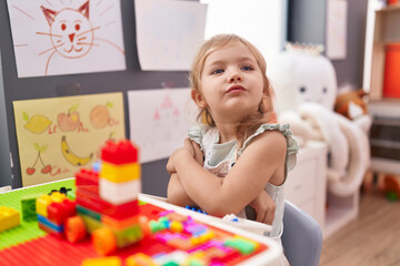 Adorable blonde girl playing with construction blocks sitting on table at kindergarten