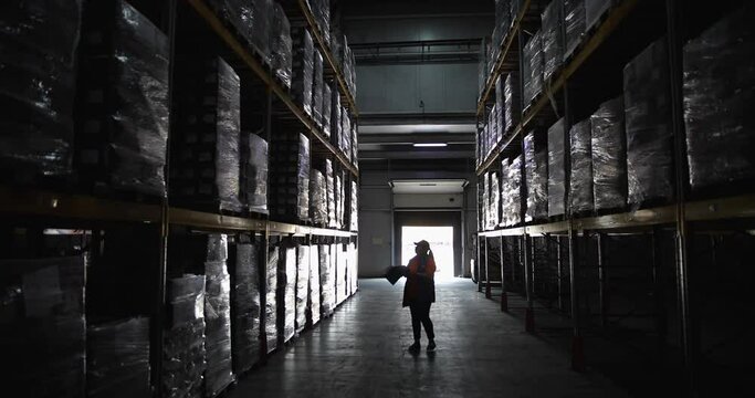 A warehouse employee examines goods stored in a large warehouse between the rows.