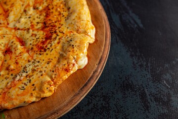 Cheese pizza on black table with abundant yellow cheese