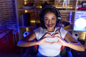 Young arab woman streamer smiling confident doing heart symbol with hands at gaming room