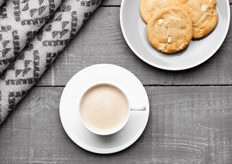 Cup of cappuccino with grey wool scarf and cookies on wooden background