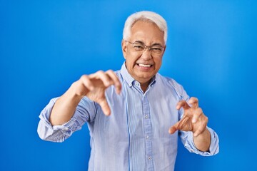 Hispanic senior man wearing glasses smiling funny doing claw gesture as cat, aggressive and sexy expression