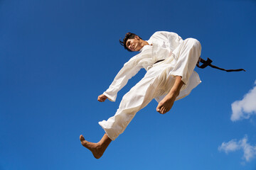 Young people, athlete, sport activity, combat and extreme sports. Hispanic man exercising in karate and traditional martial arts, jumping mid-air in the sky
