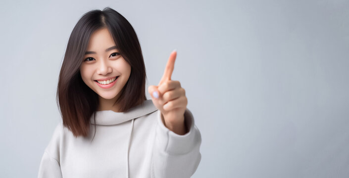 Pointing finger of an Asian girl highlights vacant space on a white background, making it a prime choice for a promotional advertising banner. Generative AI.