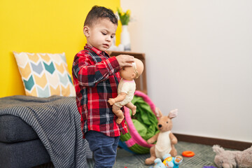 Adorable hispanic boy playing with baby doll standing at home