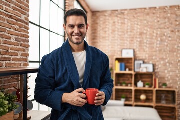 Young hispanic man wearing robe drinking coffee at home