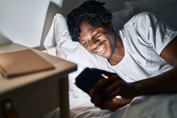 Fototapeta premium African american man using smartphone lying on bed at bedroom